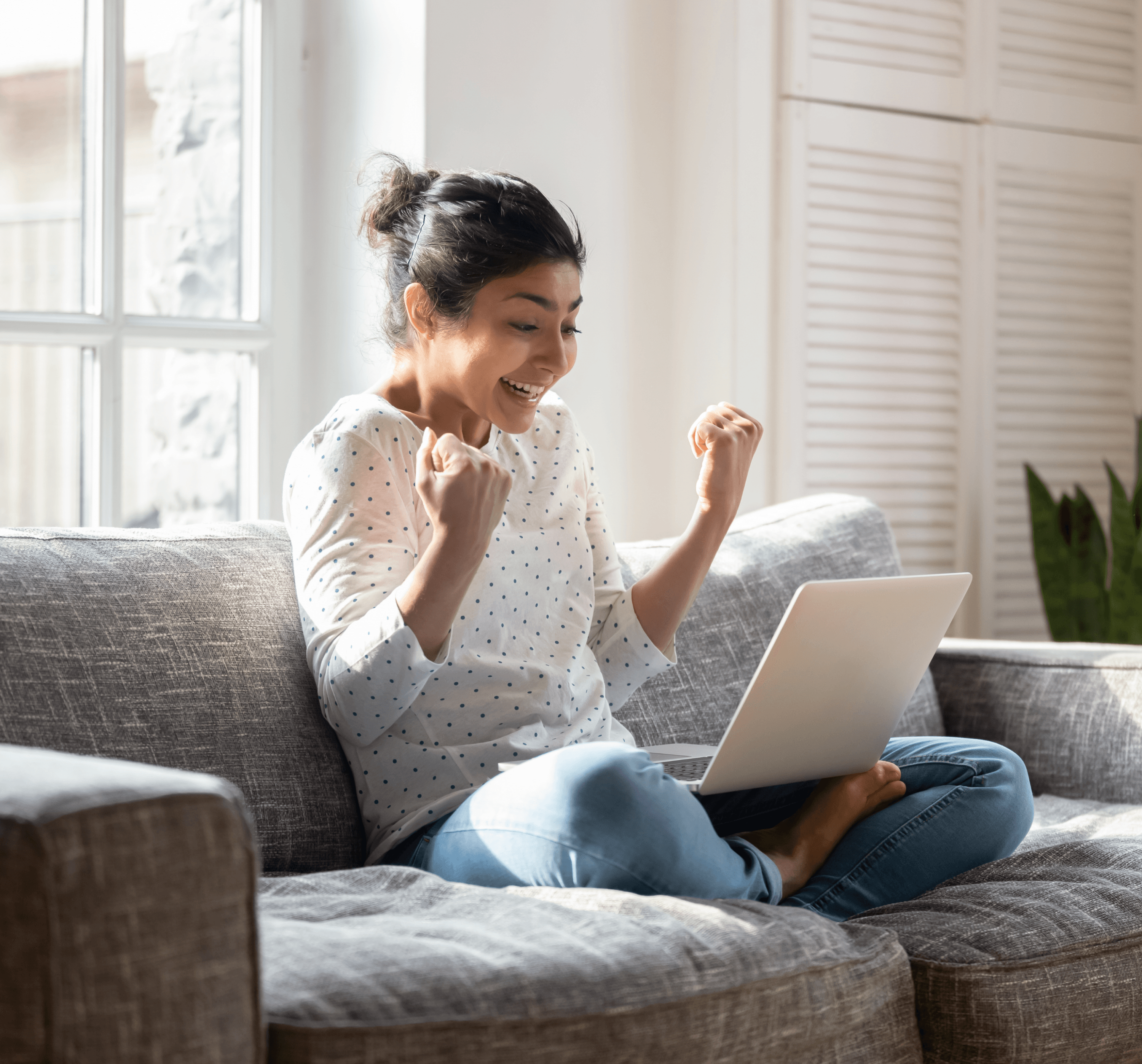 Woman on couch with laptop celebrating.