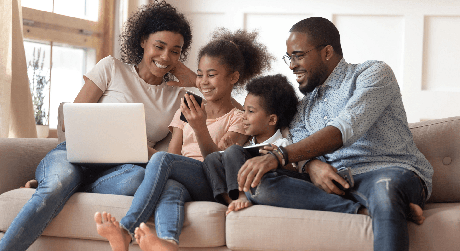 Family of four sitting on the couch looking at a laptop.